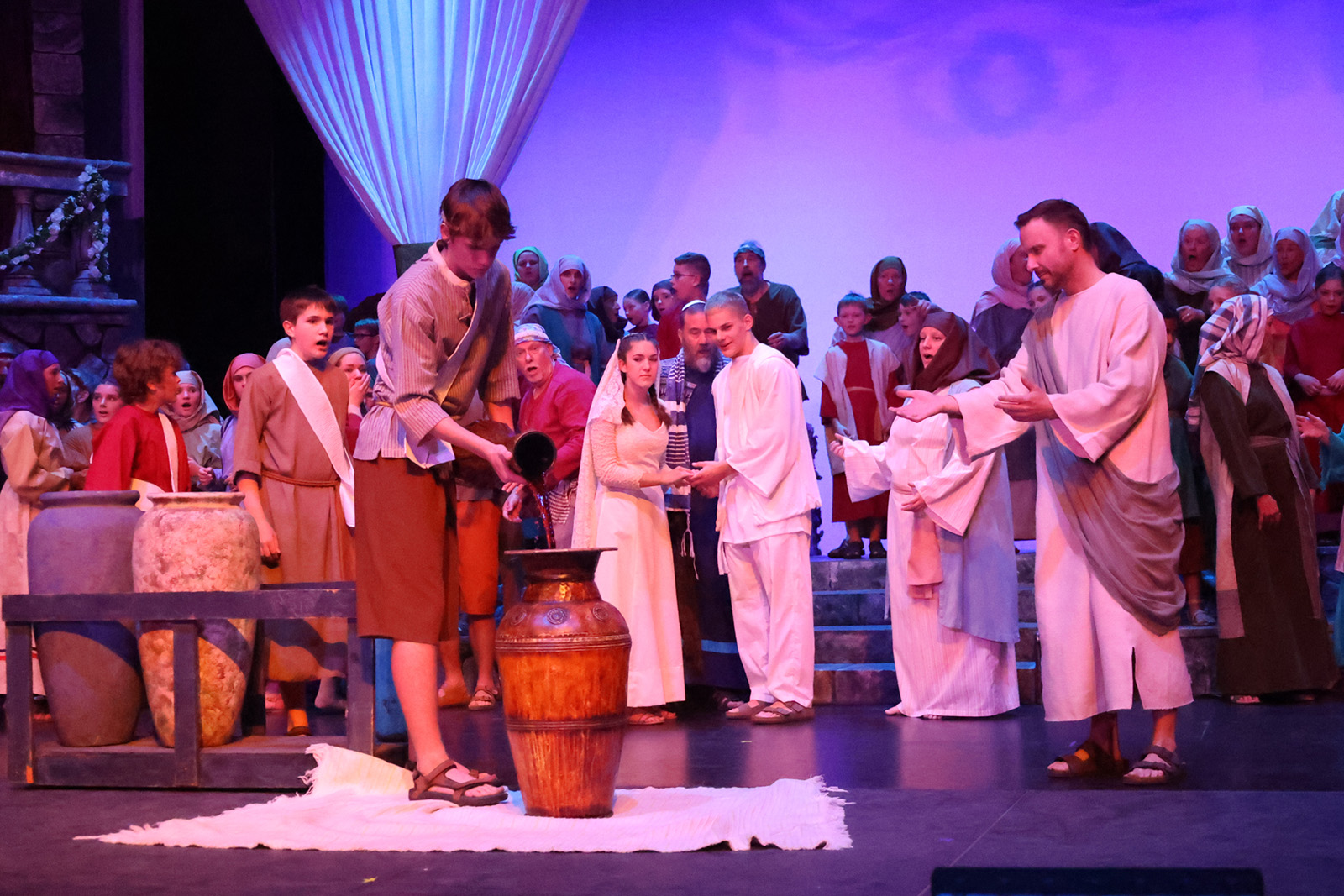 A steward pours wine as Jesus and wedding guests look on.